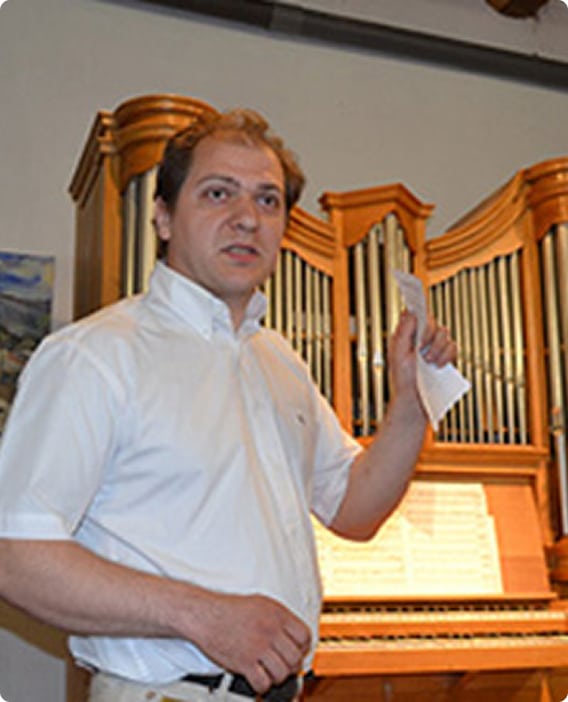 Orgue à tuyaux et musicien présentant une partition Musicien en chemise blanche tenant une partition devant un orgue à tuyaux en pleine explication.