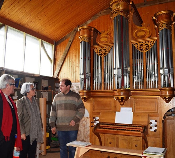 Orgue à tuyaux doré : visite d'un atelier de musique Trois personnes devant un orgue à tuyaux doré dans un atelier en bois chaleureux.